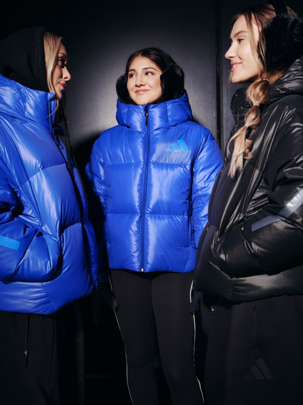 この写真には、カラフルなふっくらしたジャケットを着て暗い場所で立ち合う3人の若い女性が写っている。