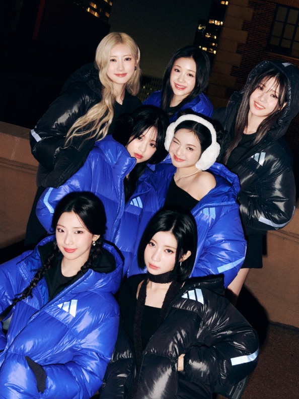 お揃いの青のダウンジャケットと黒のコートを着て、夜街の空の前で一緒にポーズを取る若い女性のグループ。