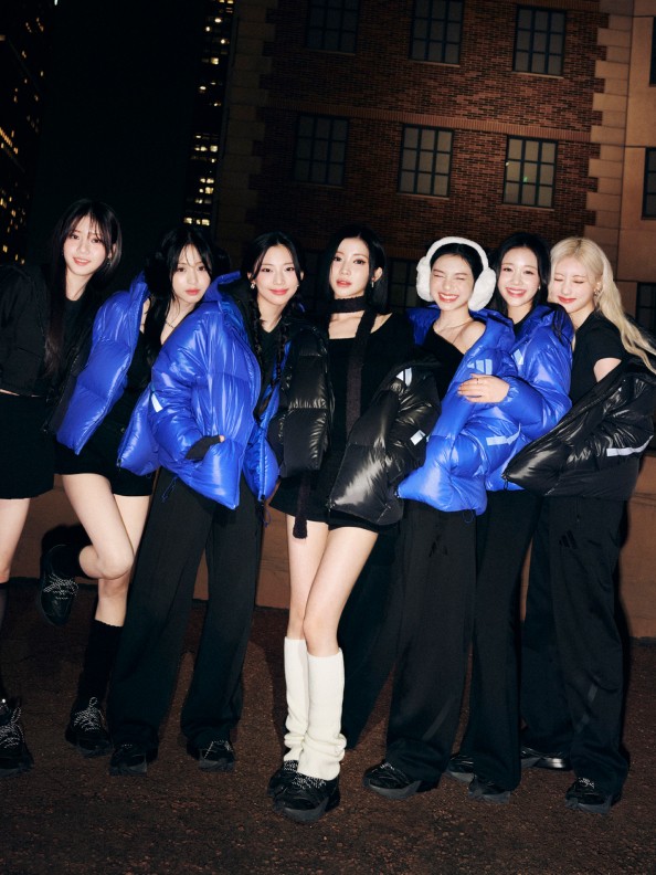 A group of young women dressed in vibrant blue and black outfits, posing together in front of a dimly lit building at night.