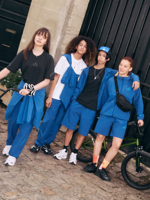 A group of young women wearing matching blue outfits, posing together in front of a dark background with a bicycle visible.