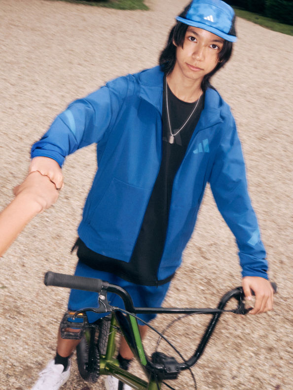 A person wearing a blue jacket and helmet is riding a bicycle on a dirt path surrounded by a grassy area.
