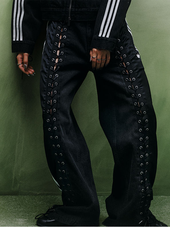 The image shows a person wearing black pants with a laced design, standing in front of a green background.