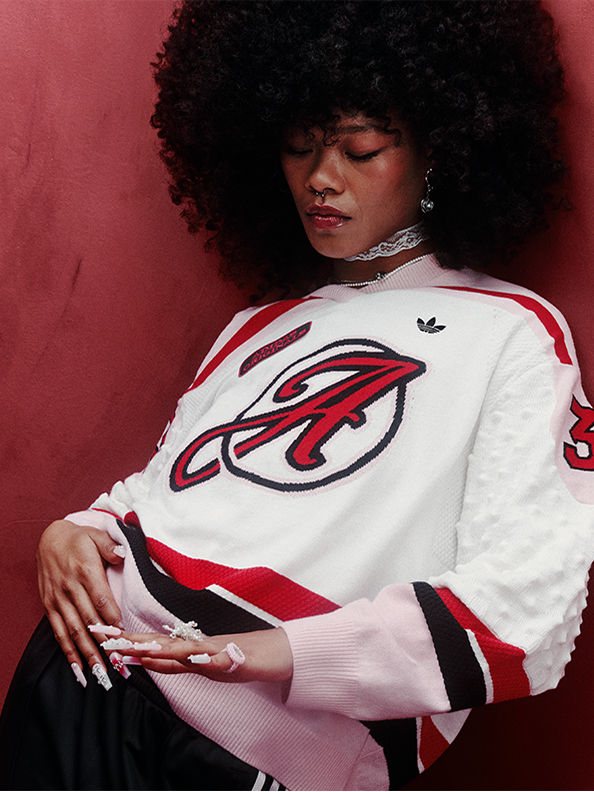 A young person with curly hair wearing a white and red sports jersey, sitting against a vibrant red background.