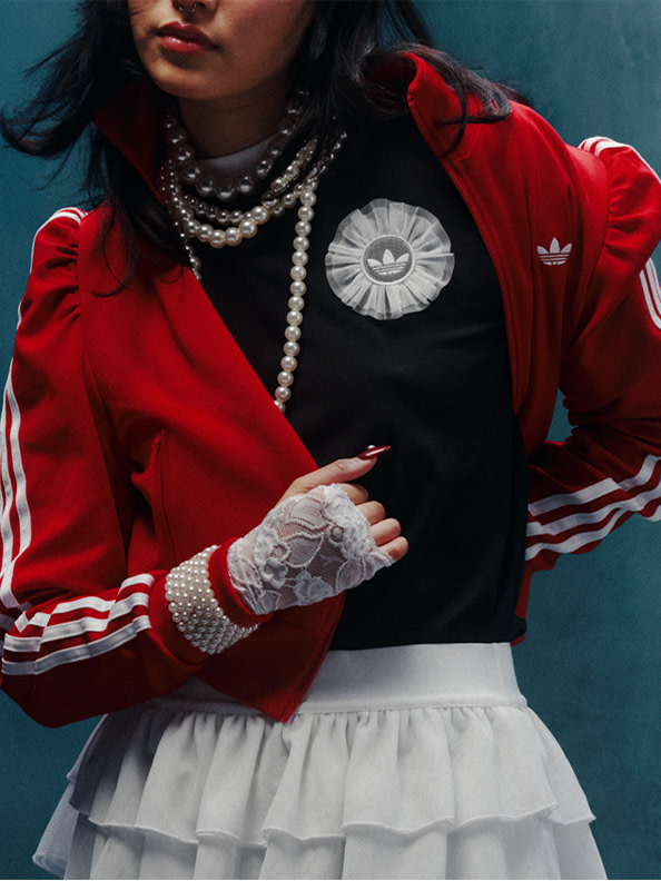 白のストライプが入った赤いジャケットを着て、黒のトップスとネックレスを組み合わせたtシャツの背景を背景にした人物のビジュアル。