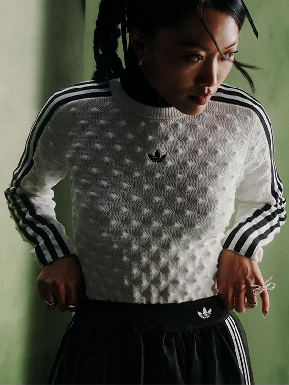 この画像では、白黒のパターンをあしらったセーターを着ている人物の手が前景に見えている。背景は暗く陰影が濃い環境のようだ。