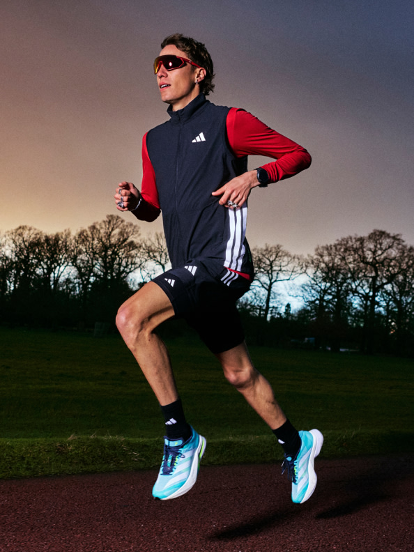 A person in athletic clothing is running on a track surrounded by trees and a sunset sky.