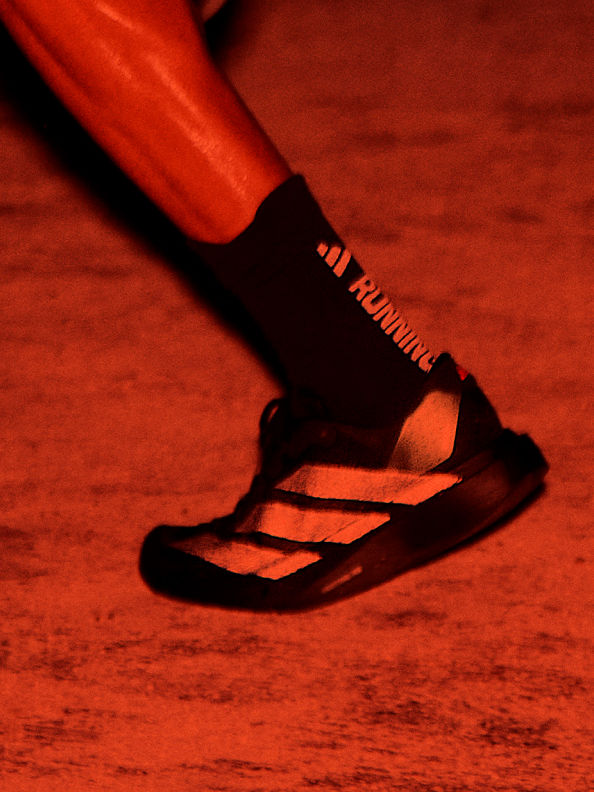 A close-up view of a person's foot wearing a red and black sandal on a reddish-orange surface.