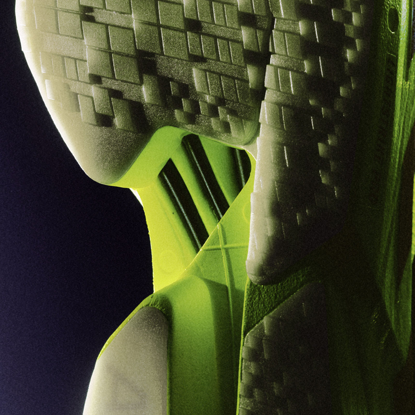 A green, abstract sculpture with geometric shapes and patterns against a dark background.