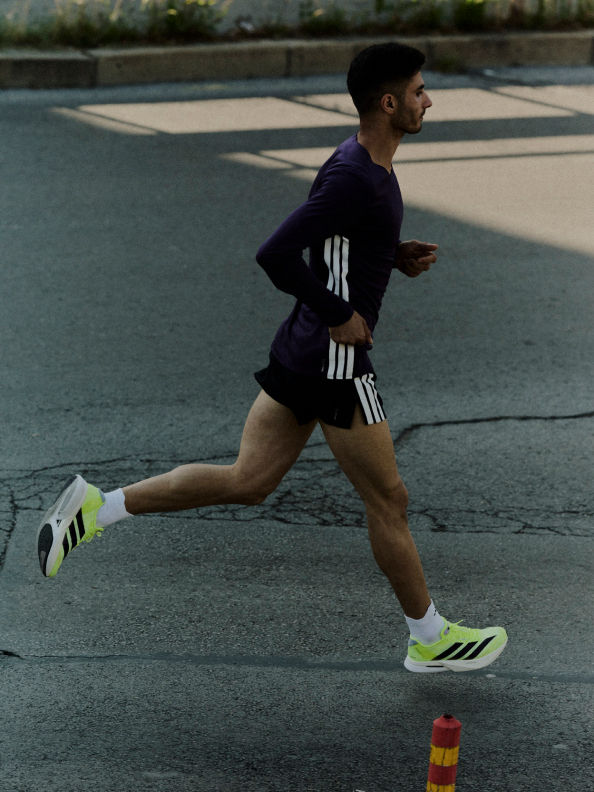 A person in athletic clothing is running on a paved outdoor court, with a blurred background of buildings and greenery.