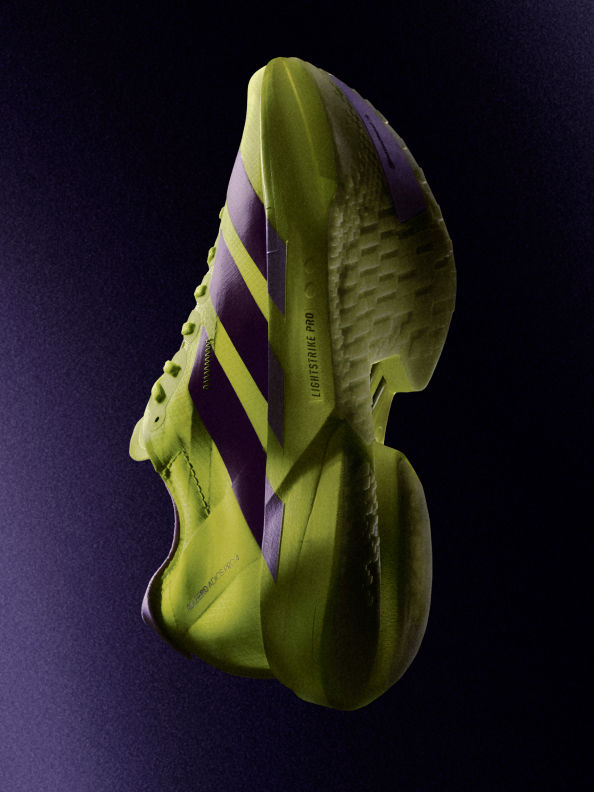 A vibrant green and purple athletic shoe stands out against a dark background, showcasing its unique design and textured surface.