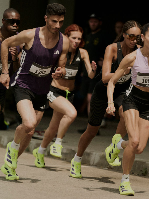 A group of runners in athletic gear are competing in a race, with the foreground showing their legs and feet as they run on a paved surface.