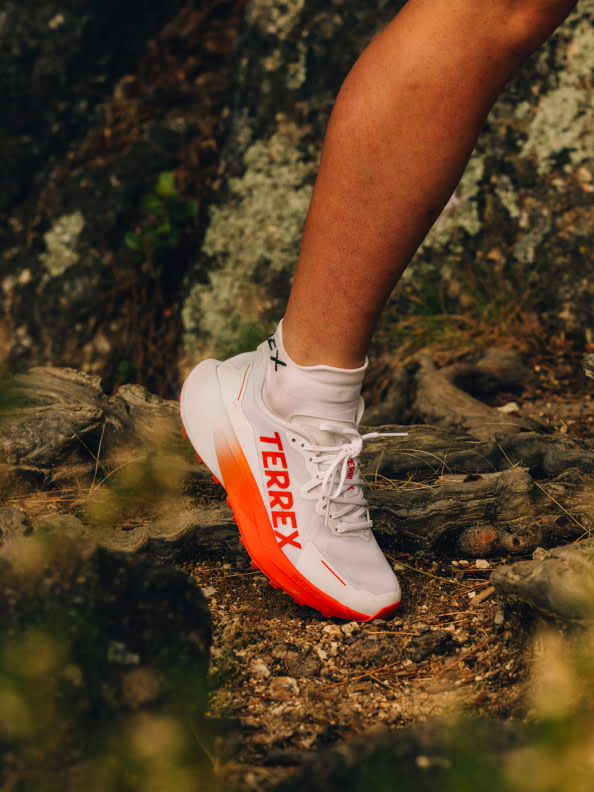 Een paar witte en oranje sportschoenen staat op een rotsachtig, besneeuwd oppervlak in een natuurlijke outdooromgeving.