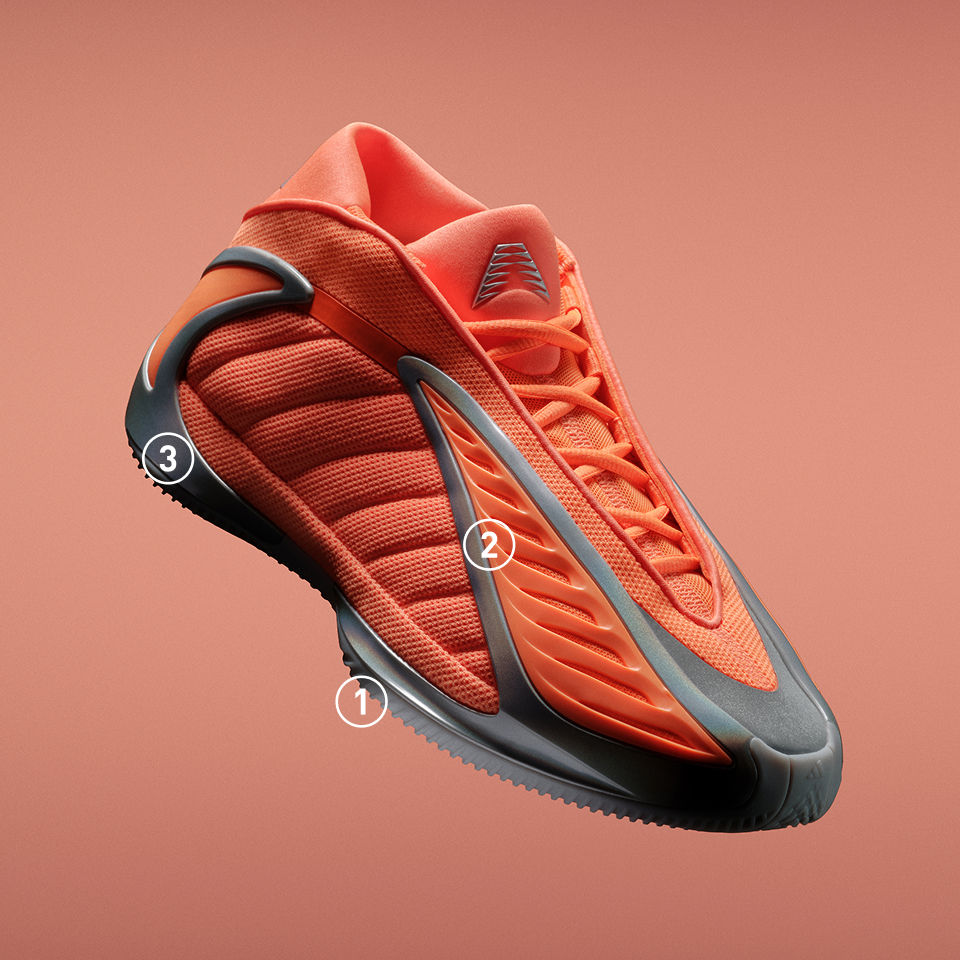 オレンジの背景に斜めに配置したオレンジとグレーのadidas Anthony Edwards 2 バスケットボールスニーカー。アウトソール、サイドパネル、ヒールに、デザインの特徴を強調する3つの番号付き吹き出しをあしらっている。