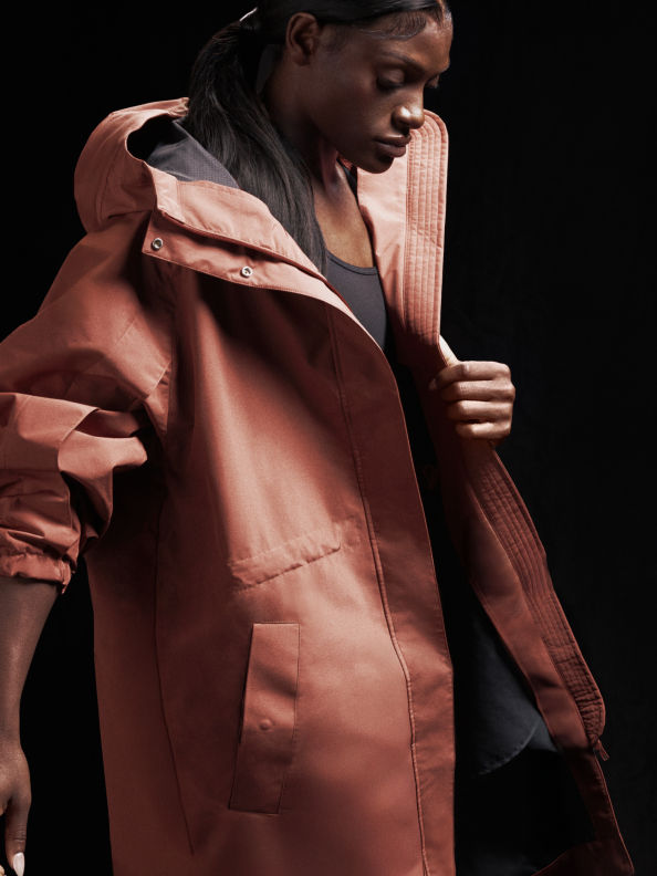 Una persona con una chaqueta con capucha de color melocotón destaca sobre un fondo oscuro con la cara parcialmente oculta.