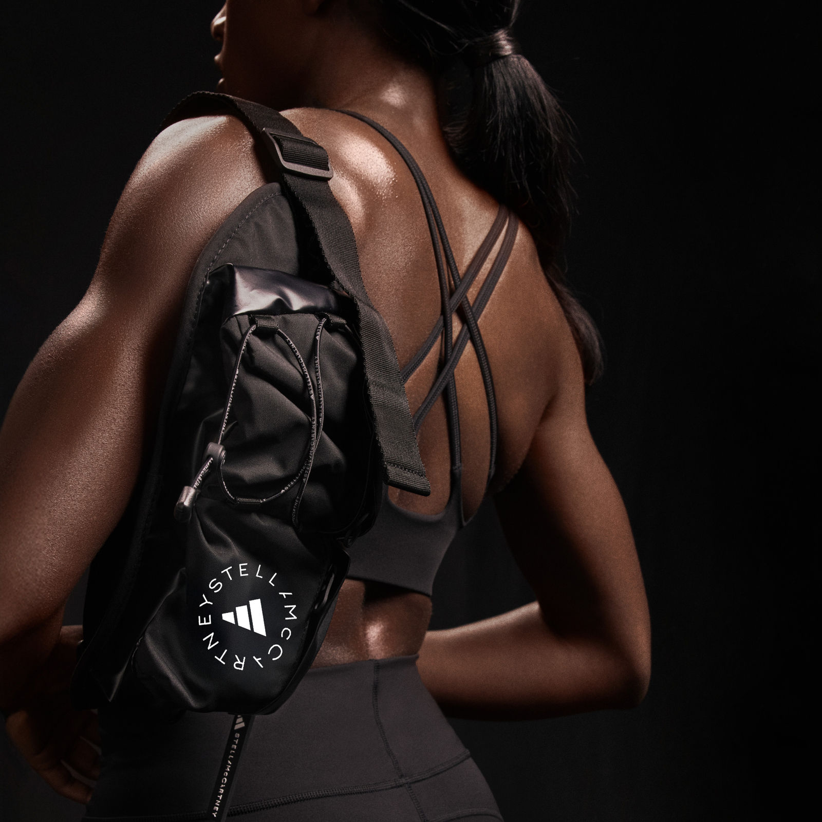 คนสวมสปอร์ตบราและกระเป๋าเป้สีดำยืนอยู่ในที่มืด มองเห็นกล้ามเนื้อหลังและไหล่ได้