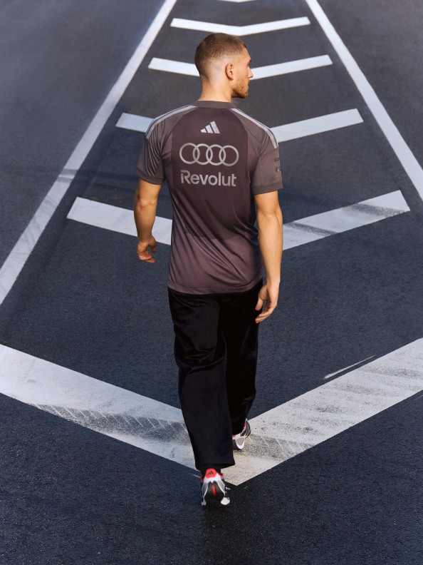 A person wearing a dark t-shirt with the Audi Revolut logo is walking on a road with white markings against a dark background.