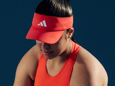 En person, der har en rød adidas-skygge og -top på, står på en mørkeblå baggrund.