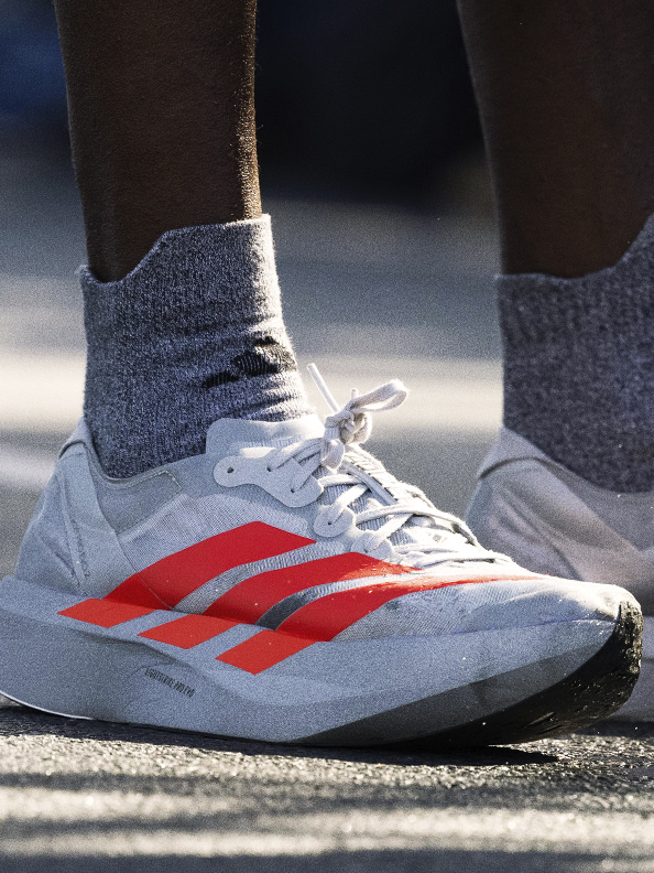 A pair of gray and red athletic shoes with white laces are visible in the foreground, set against a blurred background.