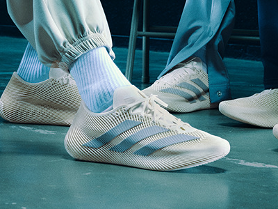 The image shows a pair of white and blue sneakers on a teal-colored surface, with a dark background suggesting a stage or performance setting.