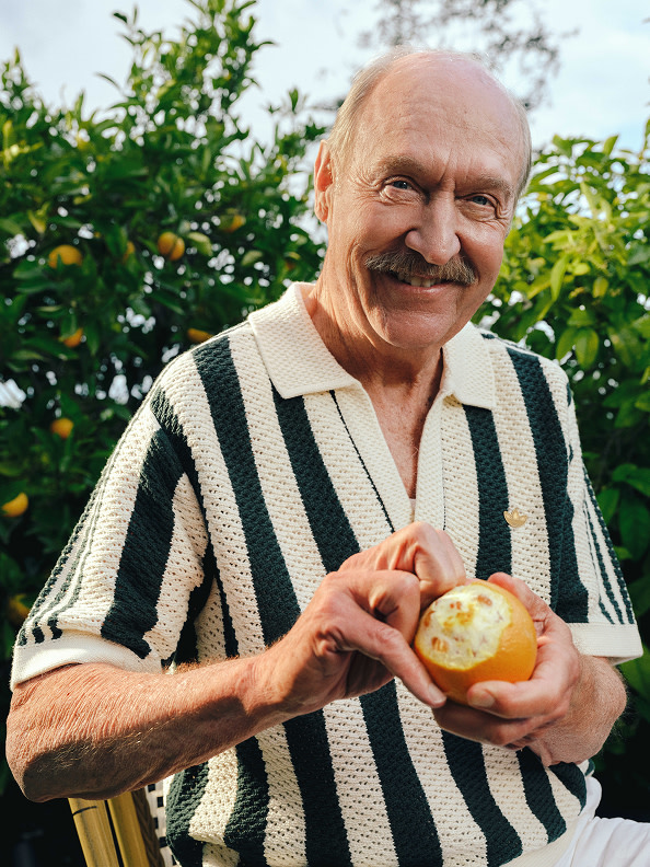 Stan Smith peeling an apple while wearing a cream and green striped shirt from the adidas x Edison Chen CLOT Stan Smith Collection. A small Trefoil is embroidered on the shirt.