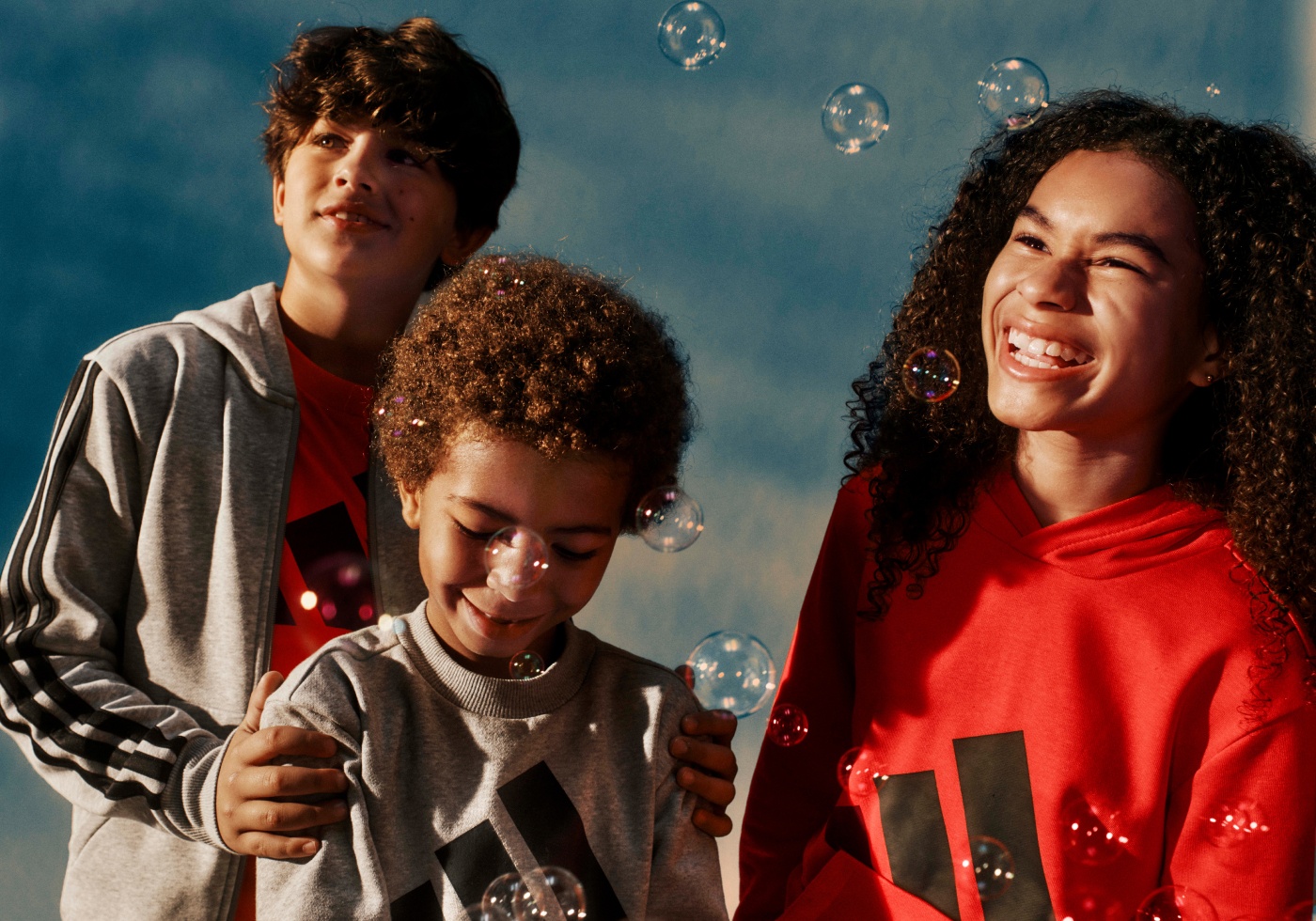 Three young individuals, two boys and one girl, are captured in a joyful moment, surrounded by bubbles against a blue background.