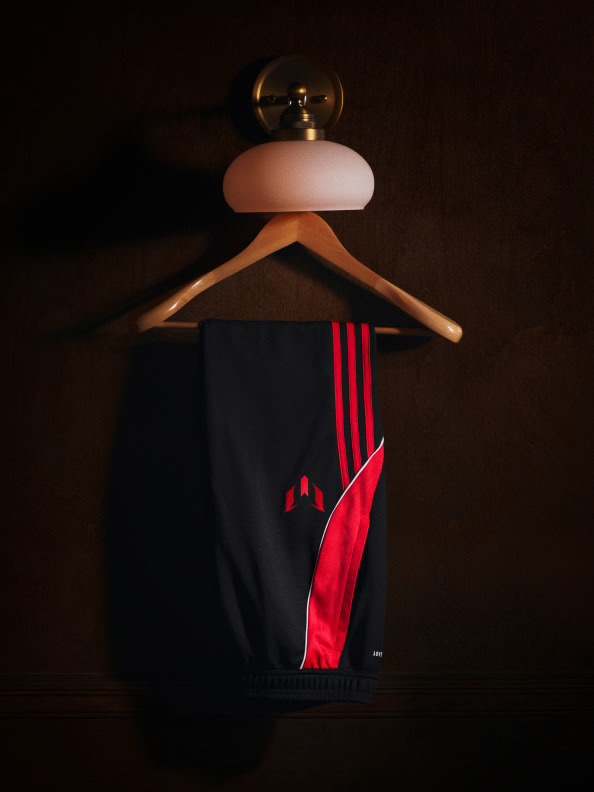 A wooden hanger with a black and red athletic shirt hanging from it, illuminated by a lamp in a dark background.