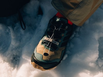 A close-up view of a person's foot wearing a rugged, multi-colored hiking boot, standing in deep snow against a dark, cloudy background.