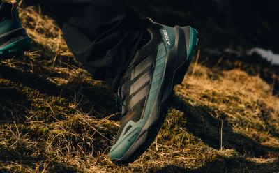 A close-up view of a pair of athletic shoes with a distinctive design, set against a backdrop of lush, grassy terrain bathed in warm, golden light.