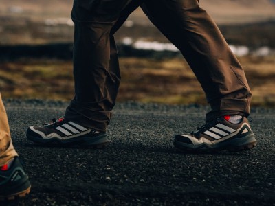 Η εικόνα δείχνει το κάτω μέρος του σώματος και των ποδιών ενός ατόμου, φορώντας ένα ζευγάρι μαύρο παντελόνι και γκρι και λευκά αθλητικά παπούτσια, που στέκονται σε ένα λιβάδι με ένα θολό φόντο.