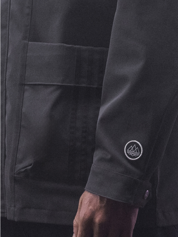 袖に小さな円形エンブレムが付いた、ダークスーツジャケットを着た人の腕の拡大図。