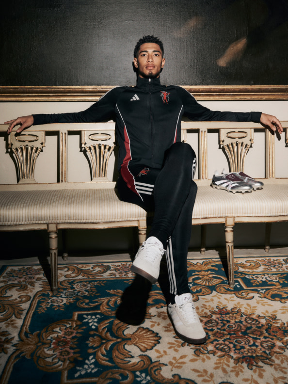 Jude Bellingham in a black and red athletic jacket sits on an ornate, patterned couch in a lavish, dimly lit room.