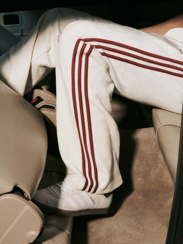 Somebody wearing white joggers with red stripes sitting in a vehicle, partially obscuring the view of the seats and other details in the background.