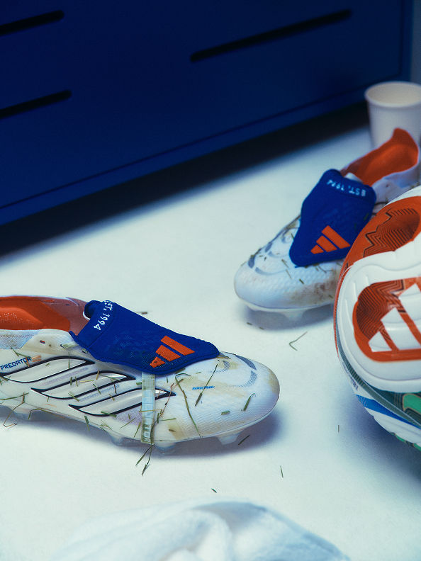 The image shows a pair of white and orange sports shoes with blue and orange accents, resting on a blue surface.