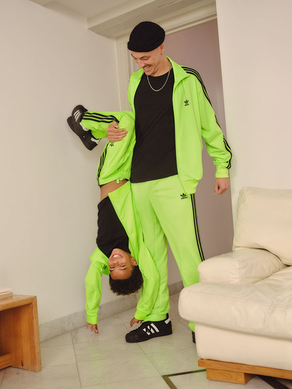 A person wearing a bright neon green tracksuit is standing in a room, with a couch and other furniture visible in the background.