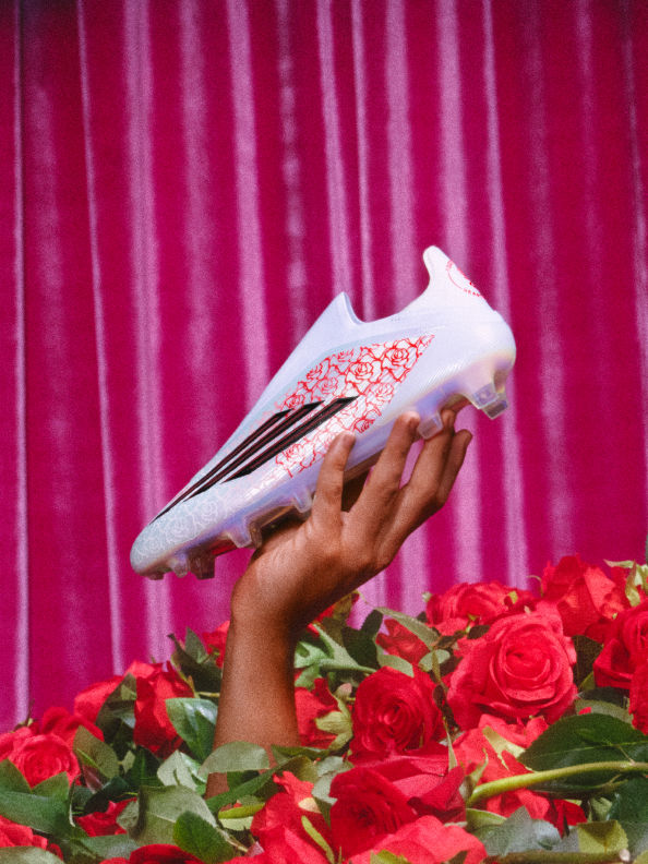Lamine Yamal’s adidas F50 shoe crushes a red rose on a glossy black floor, showing off its white, red, and black design.