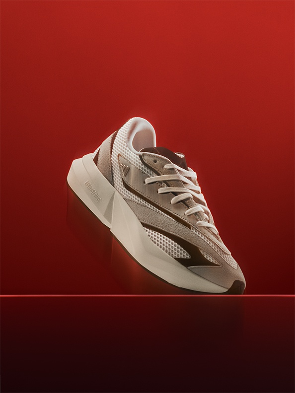 A white and gray athletic shoe with a red sole sits on a vibrant red background.