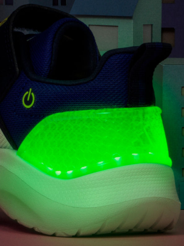 어두운 조명이 설치된 실내 경기장 표면에 놓여있는 네온 그린 컬러의 스니커즈로 어두운 블루 톤으로 물든 아웃솔을 선보입니다.