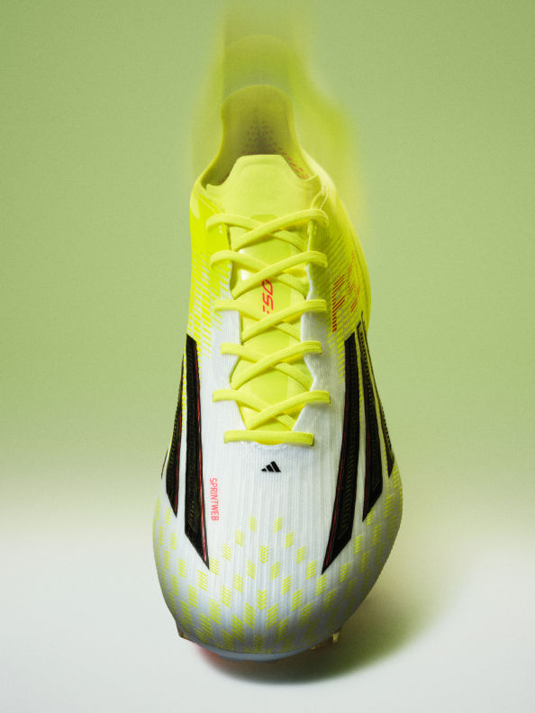 A close-up view of a bright yellow and white athletic shoe with black accents, set against a plain green background.