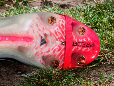 A vibrant red and white soccer cleat rests on a grassy surface, surrounded by lush greenery.
