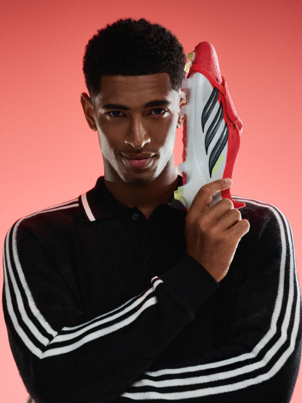 A young man with a serious expression holds a red and white athletic shoe in front of a solid red background.