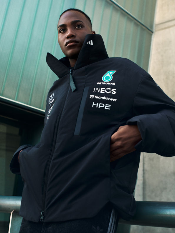 Hình ảnh này cho thấy một người mặc áo khoác đen với logo INEOS HPE, đứng trước bức tường màu teal.