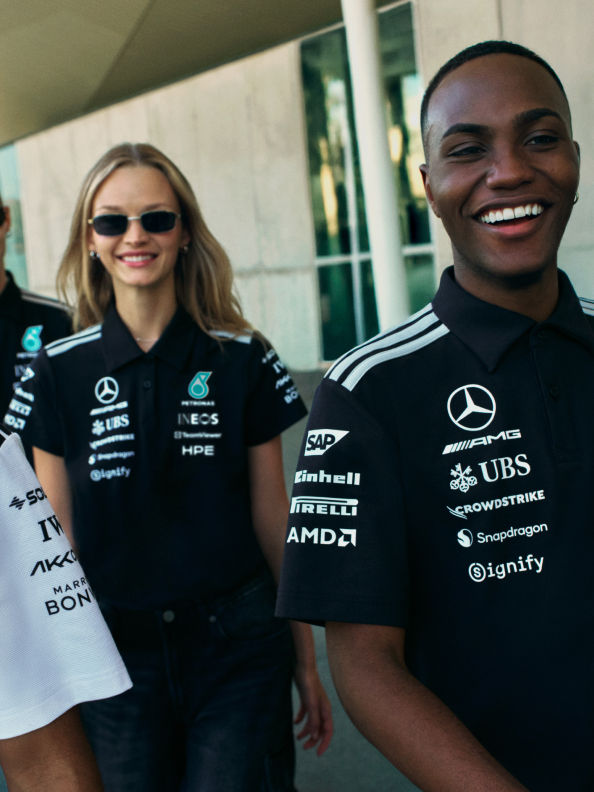 Hình ảnh này cho thấy hai người, một phụ nữ và một người đàn ông, mặc áo sơ mi đen với nhiều logo doanh nghiệp và tài trợ in trên đó. Chúng có vẻ như đang đứng trước tòa nhà hay cấu trúc với cửa kính.