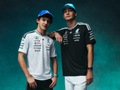 Two young men wearing sports jerseys and caps stand together in front of a teal background.