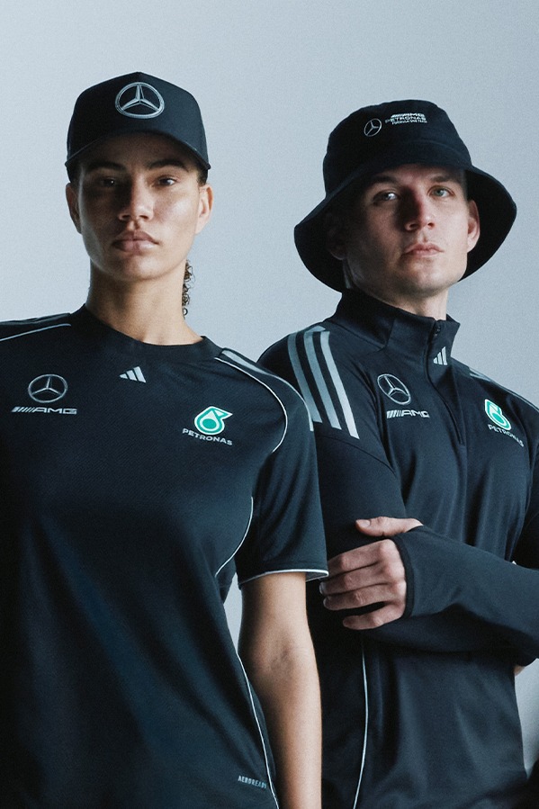 Two individuals wearing black Mercedes-Benz team uniforms and hats, standing in front of a plain background.
