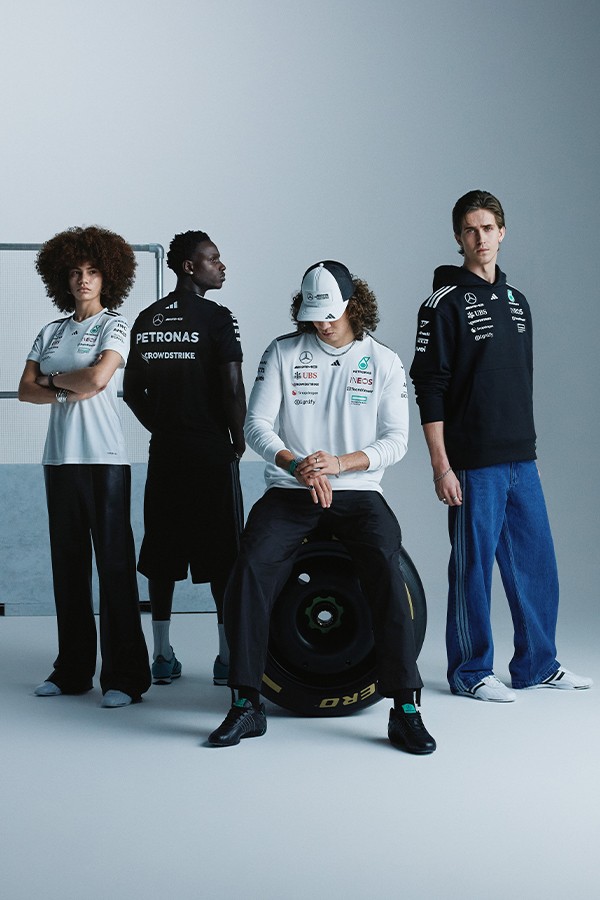 The image features a group of individuals, including a person seated in the center wearing a white uniform, surrounded by others in casual and racing attire, all standing in front of a plain background.