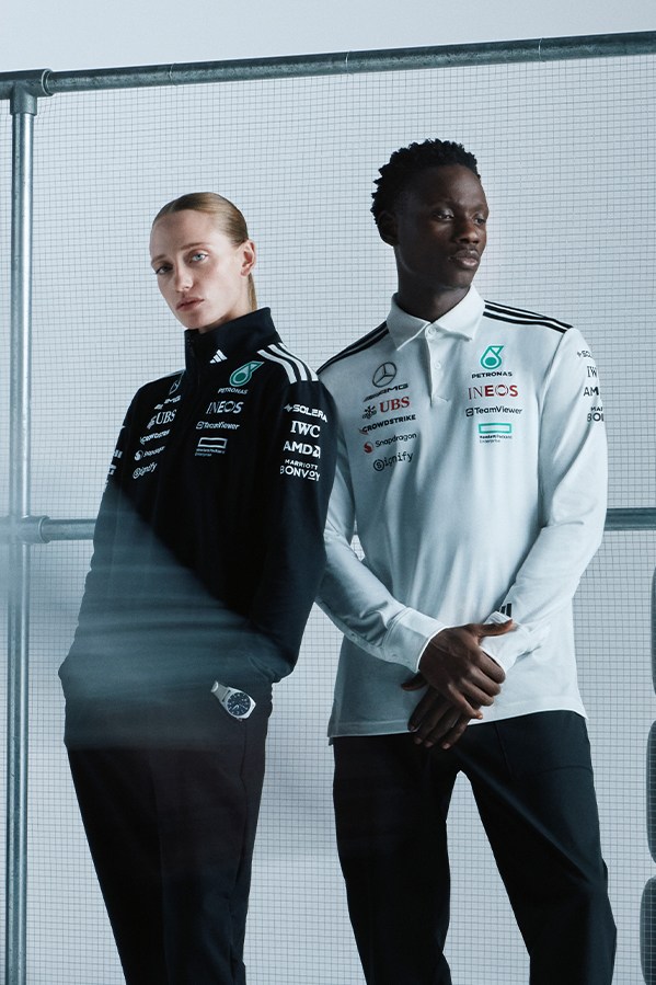 Two individuals, a man and a woman, are standing together in what appears to be a professional or sports-related setting, with a glass wall or partition in the background.