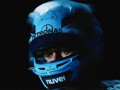 A close-up view of a racing driver's helmet, featuring the Petronas logo and the word "Nuvel" prominently displayed against a dark background.
