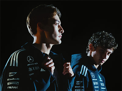 Two young men wearing sports jerseys, one with a serious expression and the other with a more relaxed demeanor, stand against a dark background.