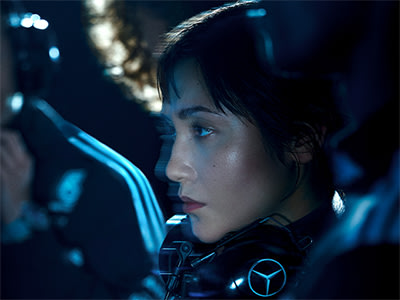 A person with dark hair is shown in close-up, their face illuminated by a blue-tinted light, creating a moody and atmospheric scene.