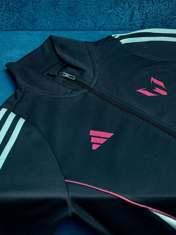 Chiếc áo khoác thể thao adidas Messi màu đen nằm phẳng phiu trên ghế bê tông.